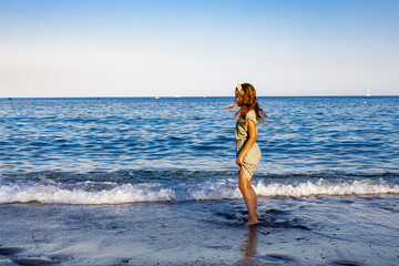 A small girl standing on the seashore, looking at the waves with curiosity and joy