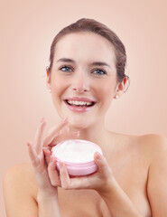 Smiling young woman with makeup holding an open plastic jar of face cream near her face. Skincare...