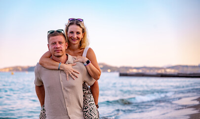 A woman on a man's back, giving him a piggyback ride, both hugging each other and laughing joyfully, on a sunny beach