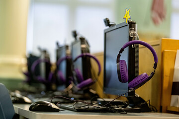 Modern school computer lab with purple headphones hanging on monitor stands with multiple desktop computers arranged in rows. Technology-enhanced learning environment showcasing digital education.