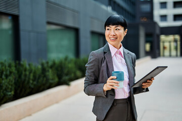 Portrait of a young asian japanese businesswoman woman using a tablet computer and holding a cup of...