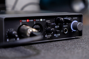 Compact black audio interface with various control knobs, input ports, and text labels like PHONES...