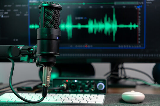 Black studio microphone with glowing green audio wave visualizer on computer monitor, representing professional podcasting, voice recording, and sound engineering