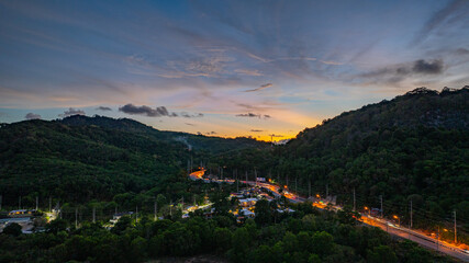 Aerial hyper lapse view of A breathtaking sunset paints the sky in vivid hues of orange and blue over a coastal town, with lush green hills framing the scene. cloud in dramatic sunset over the ocean