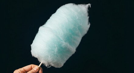 A hand holding a large blue cotton candy on a stick against a dark background in a studio shot