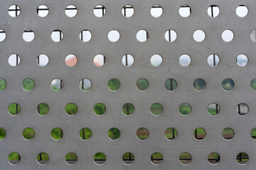 Gray metal plate with a grid of perfectly aligned circular holes. Perforated steel sheet creating an abstract, industrial, and modern pattern background.