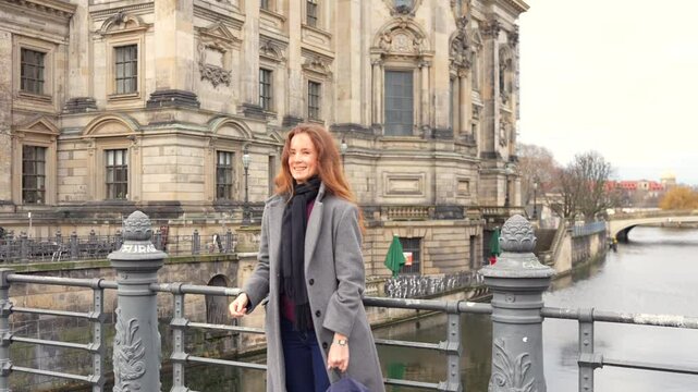 Woman tossing a coin into the Spree River near Berlin Cathedral, following a travel tradition for good luck and return, with historic architecture and winter scenery in the background