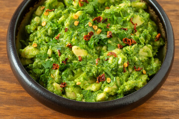 Homemade avocado salsa (guacamole) sprinkled with hot chili flakes in a bowl on a brown wooden table. 