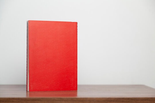 A red book on a wooden table. Book concept. Knowledge concept. 
Space for text.