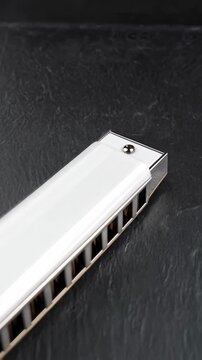 Close-up of white diatonic harmonica on textured dark background, musical instrument for blues, folk and country music