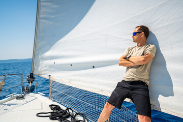 Man leaning on full sails of a sailing yacht in the open sea near Croatia. Masculinity, leadership,...