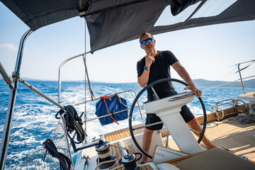 Man standing at the helm of a sailing yacht near Croatia, steering the boat through open water....
