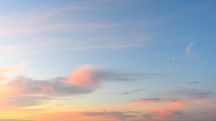 Soft pink and orange clouds drift across a calm blue morning sky as the sun begins to rise.
