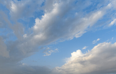Thick white and gray clouds move across a bright blue sky in the early morning light.