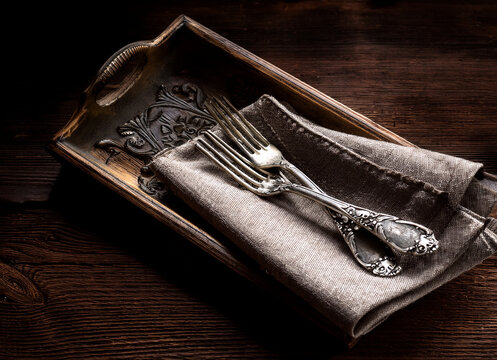 altem Silberbesteck mit Ornamenten auf einer Leinenstoff Serviette, in einem dunklen Holztablett