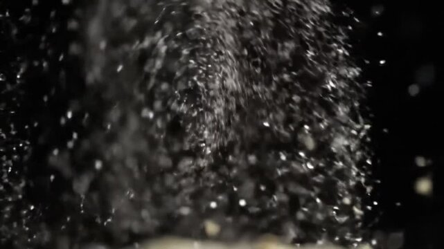 Natural organic dust particles floating on a black background. Glittering and sparkling particles gently spinning in the air with soft bokeh. Dynamic motion mix of fast and slow movement. Shimmering, 