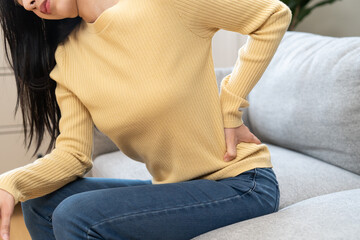 Close-up woman massaging her lower back has back pain because of sitting posture during work in...