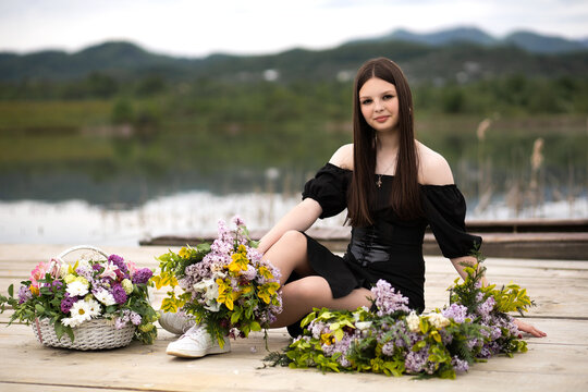 A girl in a dress sits on a pier on wooden planks, next to her is a flower arrangement