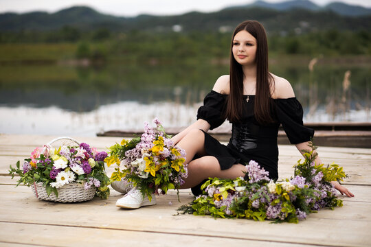 A girl in a dress sits on a pier on wooden planks, next to her is a flower arrangement