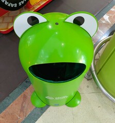 Cubo de basura con forma de rana con la boca abierta en zona infantil de centro comercial de...