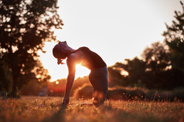 Woman practicing yoga and stretching in the park on a hot sunny summertime day.