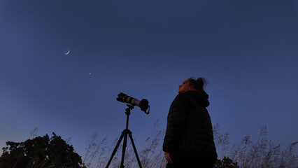 Amateur astronomer using camera and lens for photographing stars, Moon, planets and other celestial objects from a field in nature.