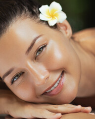 Happy Woman Resting in Spa with Glowing Skin and Tropical Flower in Hair
