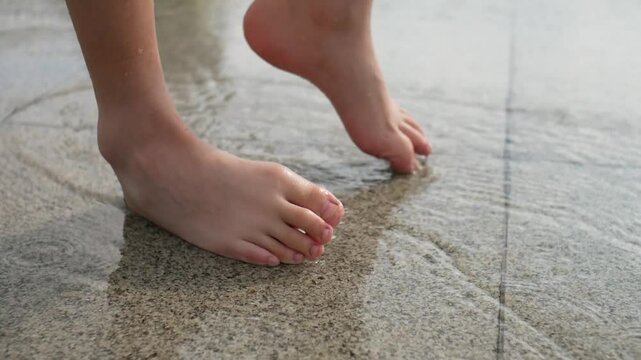 Close-up of a childs bare feet standing in a summer rain puddle on paving slabs