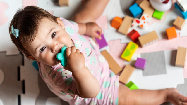 Cute baby girl playing, learning and developing with colorful educational toys. Adorable toddler chewing a sensory toy surrounded by blocks. Fun, health, childhood, creativity and play