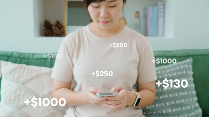 Asian woman earning money online with a smartphone, showing financial success with pop-up dollar...
