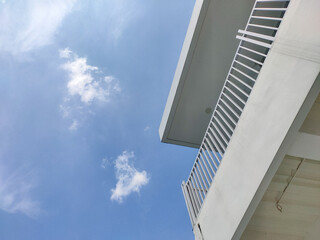 Fototapeta premium A dynamic low angle view shows the modern architectural details of a building with a clean white balcony railing under a vast blue sky with scattered white clouds.