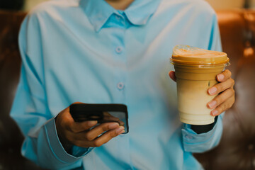 Young adult holding smartphone and iced coffee in relaxed café setting, enjoying moments of leisure and technology connection