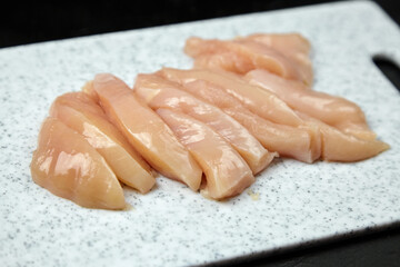 Freshly sliced raw chicken breast fillets arranged neatly on a speckled cutting board, showcasing the texture and quality of the poultry meat for culinary use