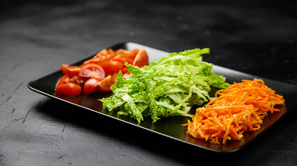 Freshly prepared vegetables including sliced tomatoes, shredded carrots, and crisp lettuce arranged on a black plate, showcasing vibrant colors and healthy eating options for culinary inspiration