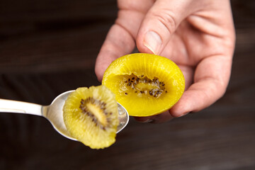 Hand holding a sliced golden kiwi fruit on a spoon, showcasing its vibrant yellow flesh and tiny...