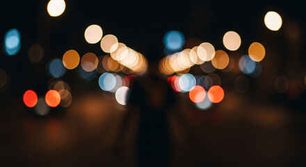 Fototapeta premium Nighttime street scene with blurred lights creating a bokeh effect, person silhouette.