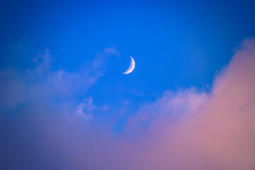 There is a white crescent moon and red clouds in the dark(deep) blue sky.
