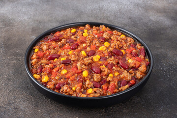 Mexican chili con carne stew with beans, corn and tomatoes on grey background. Tex-Mex cuisine.