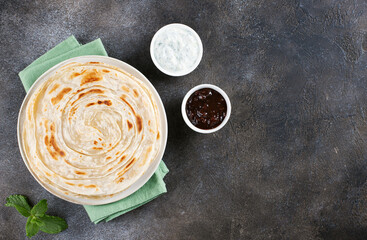 Indian flatbread paratha with raita sauce and chutney on gray background, top view. Indian food.