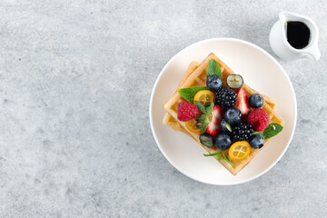 Belgian waffles with fresh raspberries, blackberries and maple syrup on gray background. Top view.