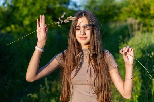 Teen with closed eyes and grass shadow on face. Teen girl stands in sunlight with eyes closed, holding dry grass that casts a dramatic shadow across her peaceful face and body.
