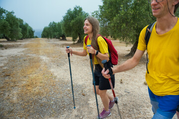 Smiling Hikers Exploring Scenic Olive Grove Landscape Together, equipped with trekking poles,...