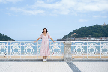 Chica joven morena con vestido rosa de verano apoyada sobre la barandilla del paseo marítimo en la...