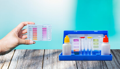 Water tester in girl hand with liquid water tester test kit on wooden table with space on clear swimming pool water background, quality water testing test kit, pool maintenance and service business co