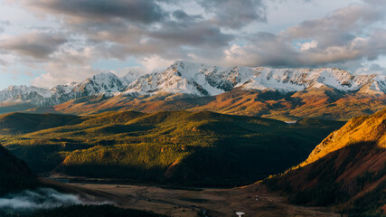 Golden hour sunlight illuminates a vast, verdant valley nestled beneath towering, snow-capped...