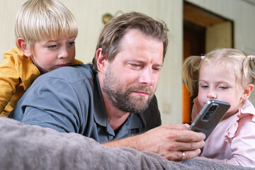 Young dad using smartphone with his kids. Man watching something in a smartphone. Happy father,...