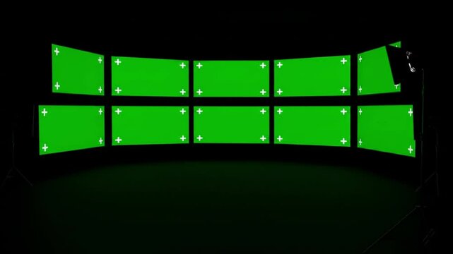 A studio setup with multiple green screens arranged in a curved formation in darkness