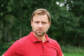 Portrait of handsome young man in a red t-shirt outdoors. Male with fair hair and beard feel happy,...