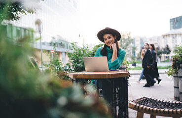 Brunette woman, 30, working on laptop in cafe garden, blending style and remote productivity with...