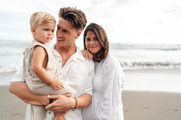 Modern family portrait on beach, child in arms, reflecting emotional intelligence datasets and digital companion tech based on body posture, facial cues, and real-life family bonding models.